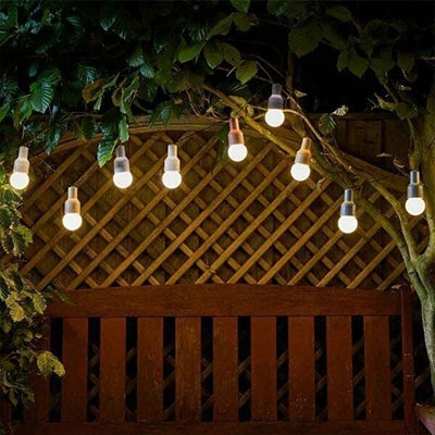 Outdoor solar lights, hanging from tree shaped as lightbulbs at night.