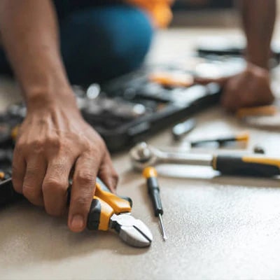 Image of a man holding a pair of pliers, with a tool box behind him.